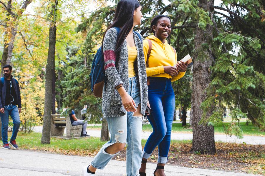 Two students walking outdoors during summer, laughing together
